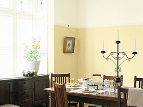 Traditional yellow dining room timber dining table with candle and dark wooden drawes with plant